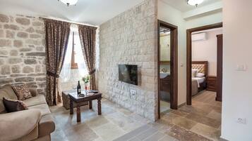 A living room with a stone wall, a flat-screen TV, a sofa, a coffee table, and a window with curtains.