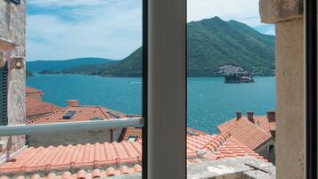 A balcony with terracotta roof tiles, a stone wall, and a view of a lake with a distant island.