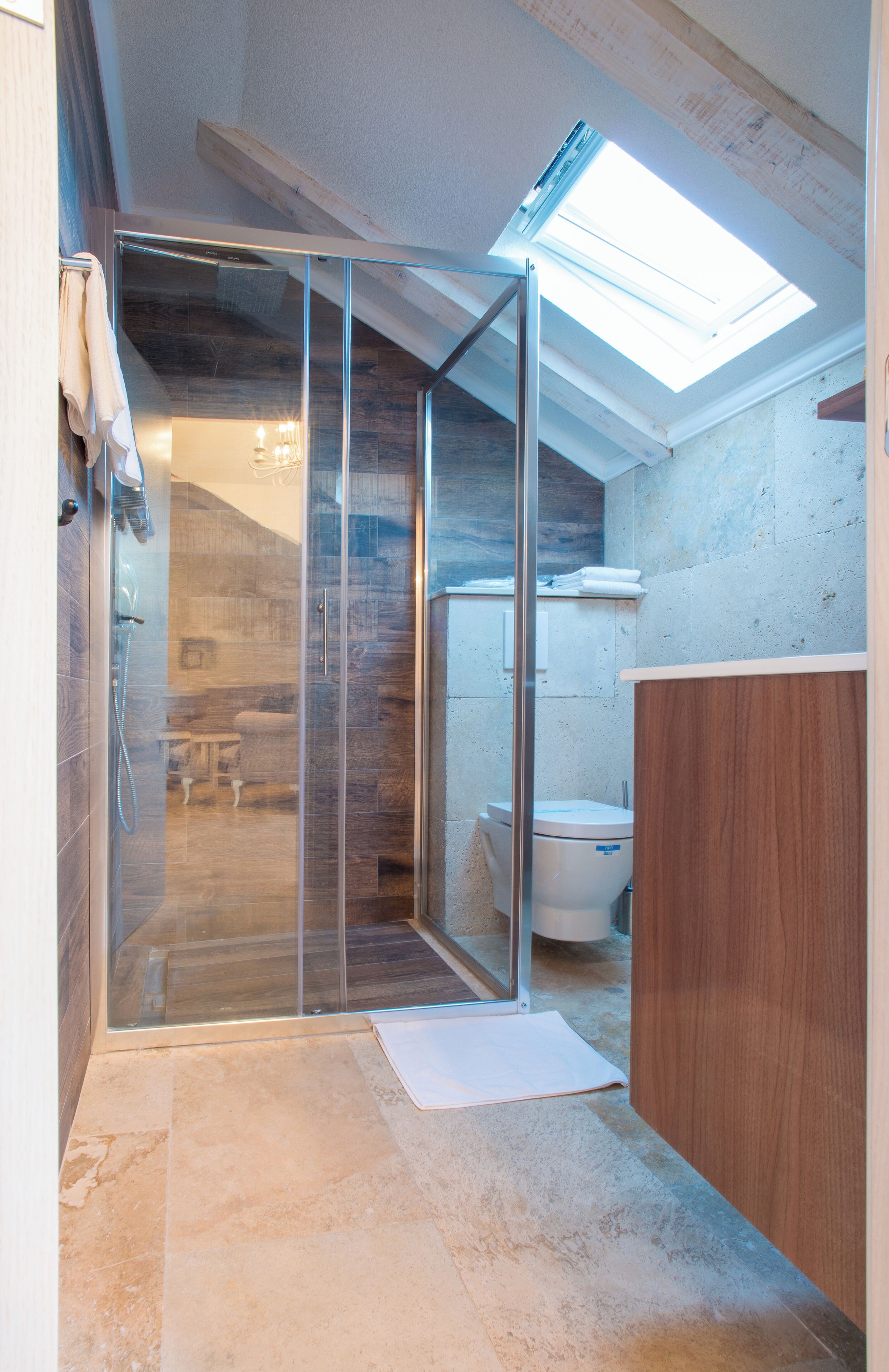 A modern bathroom with a glass shower enclosure, a wooden vanity, and a skylight.