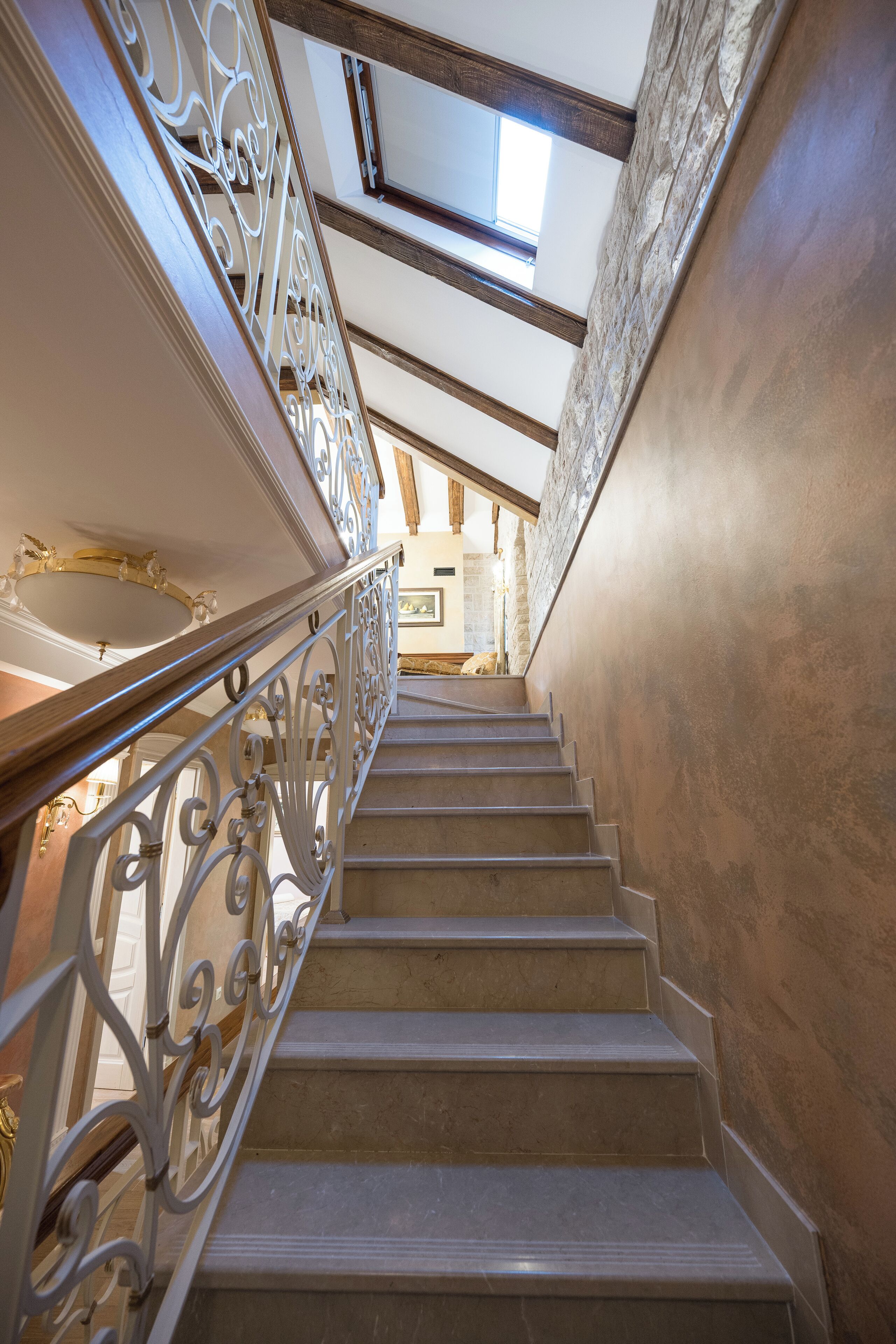 Un magnifique escalier orné de rampes en métal ouvragé, un plafond en voûte et un mur en pierre.