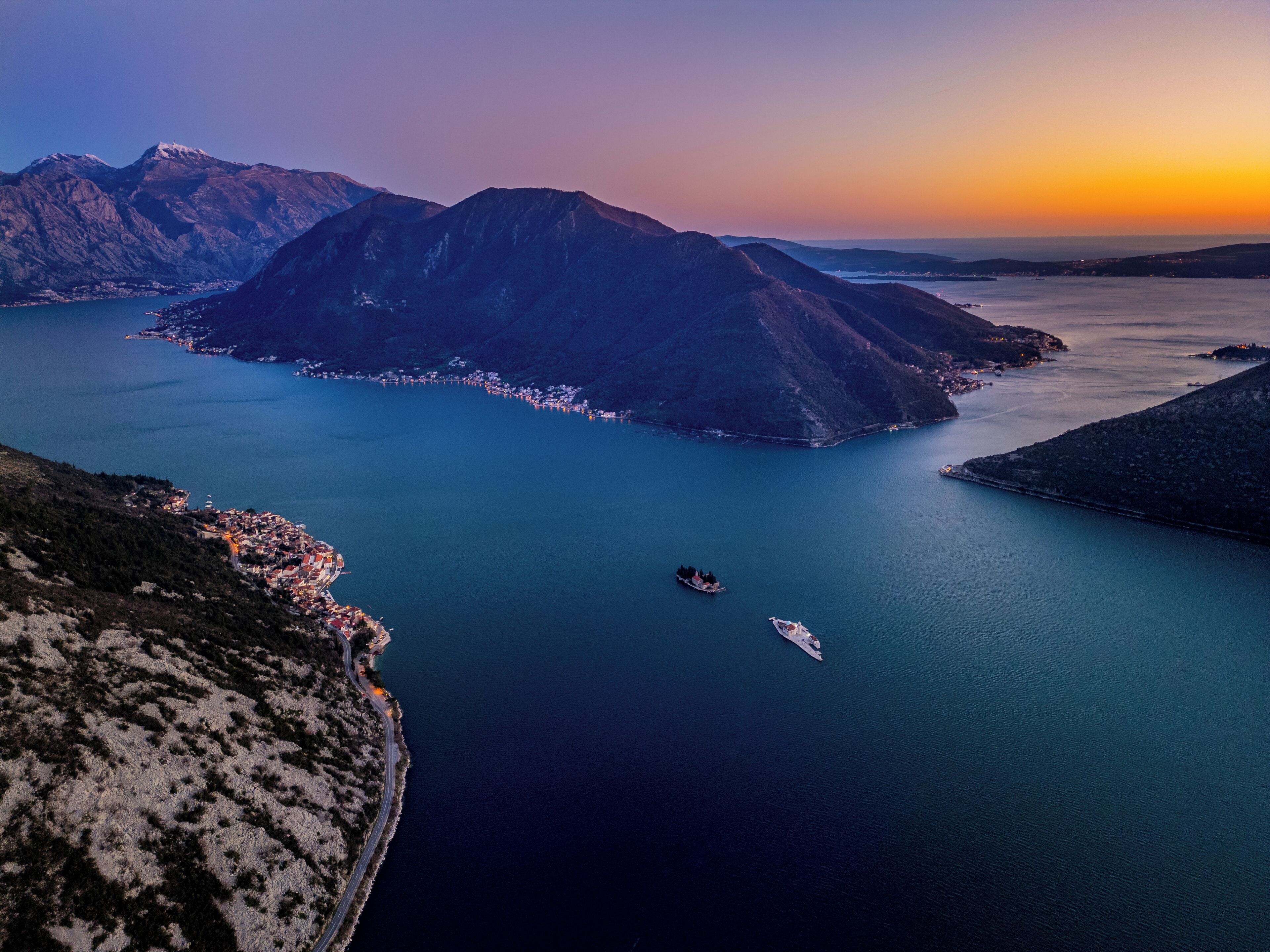 A coastal landscape with mountains, a body of water, and a small town.