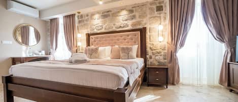 A bedroom with a stone wall, a large bed, a nightstand, and a mirror.