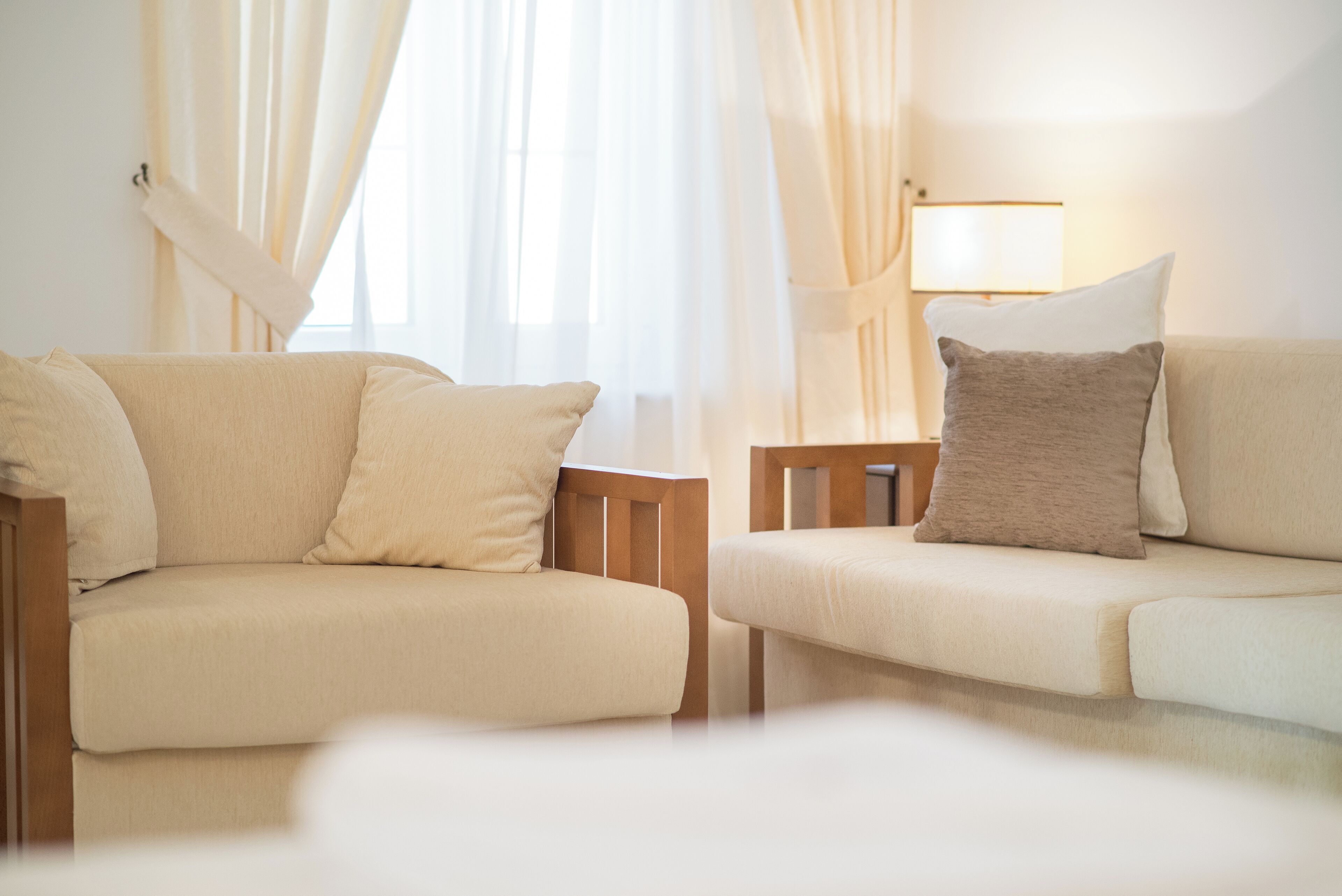A modern hotel room with two beige sofas, a wooden side table, and a lamp.