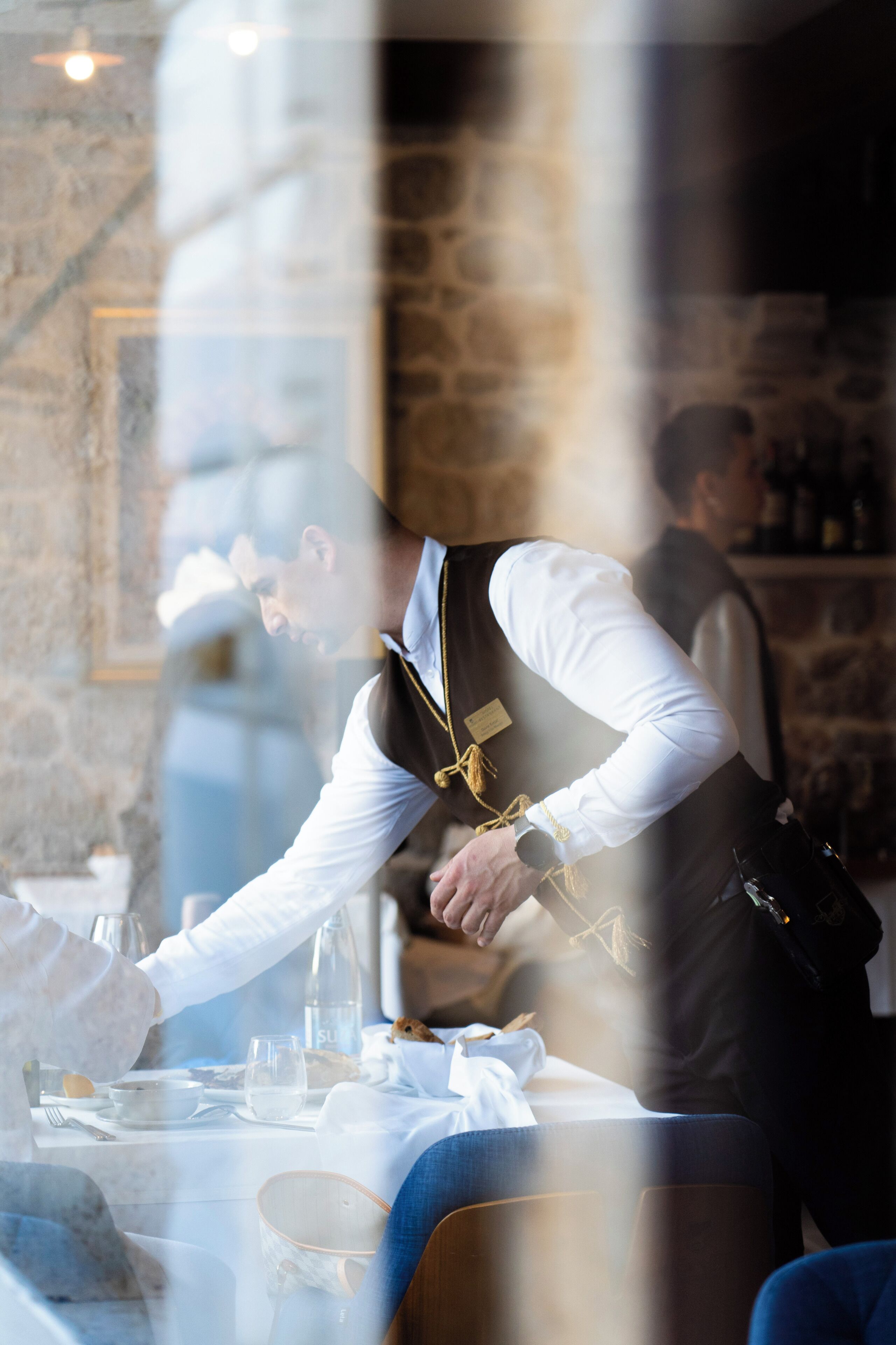A waiter serving a meal at a table with a stone wall background.