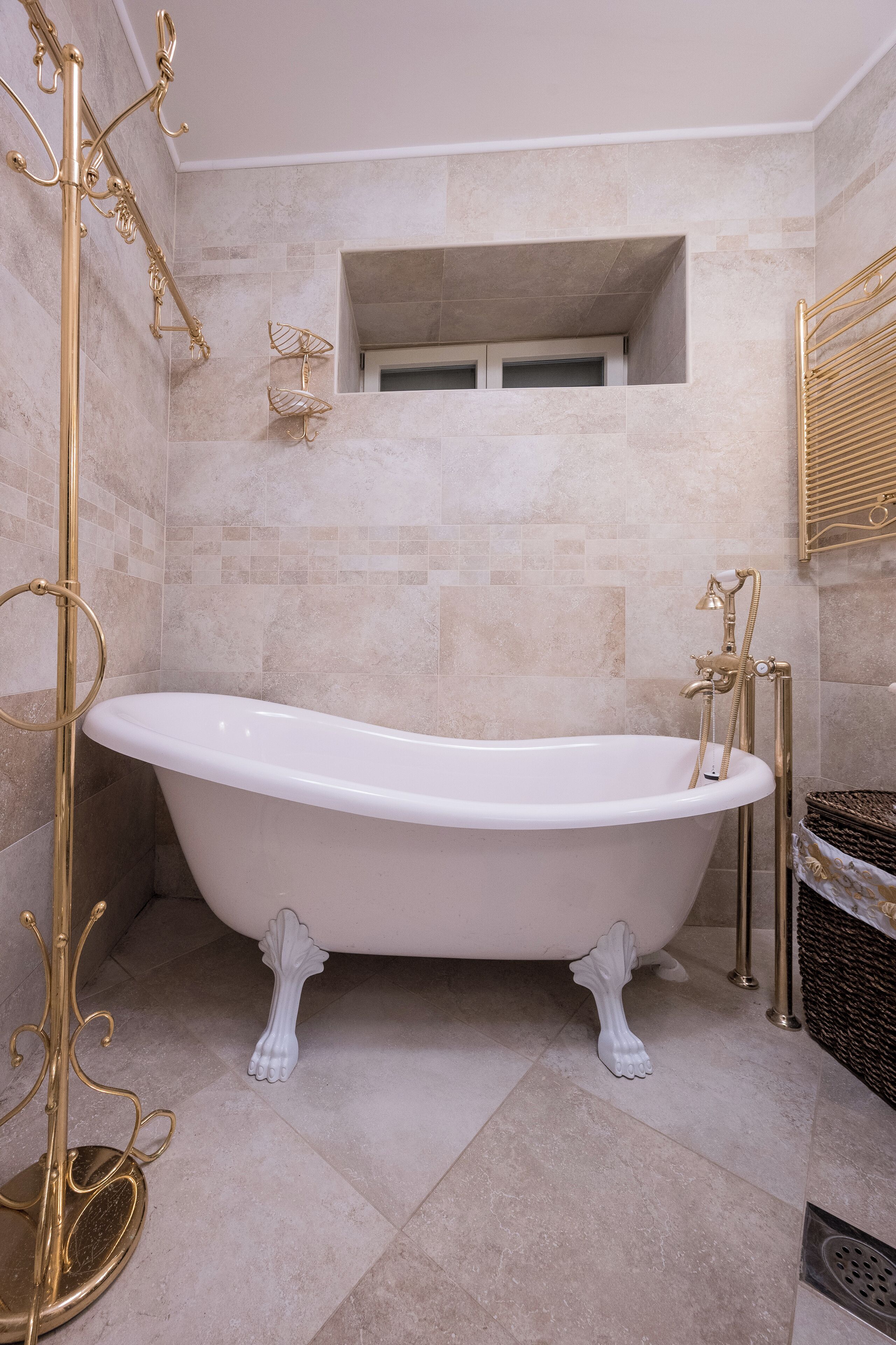 A bathroom with a freestanding bathtub, gold fixtures, and beige tiles.