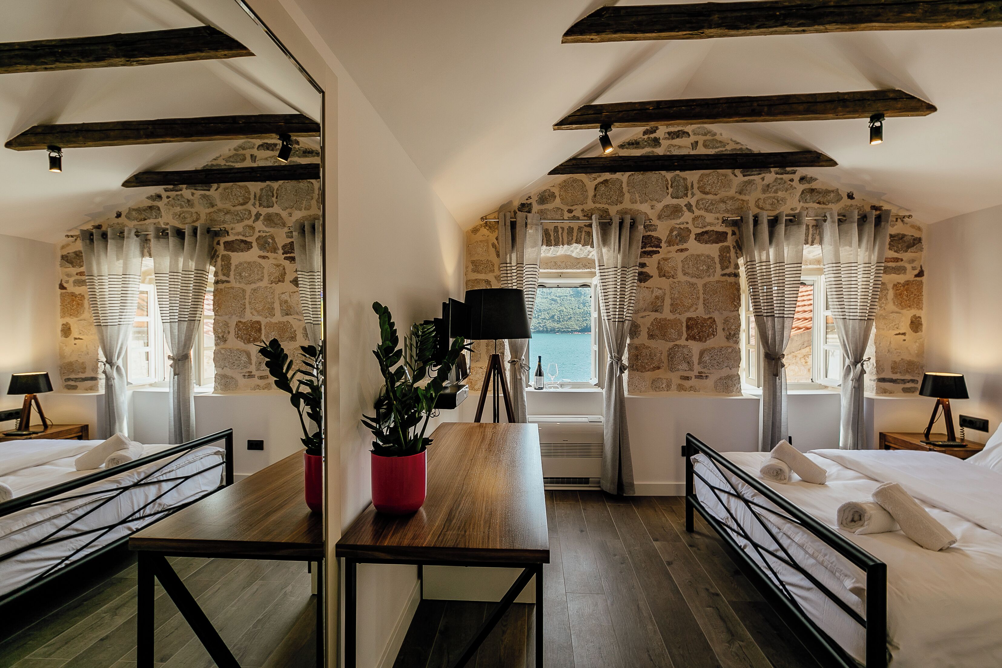 Une chambre avec un mur en pierre, deux lits, une table en bois et une plante en pot.