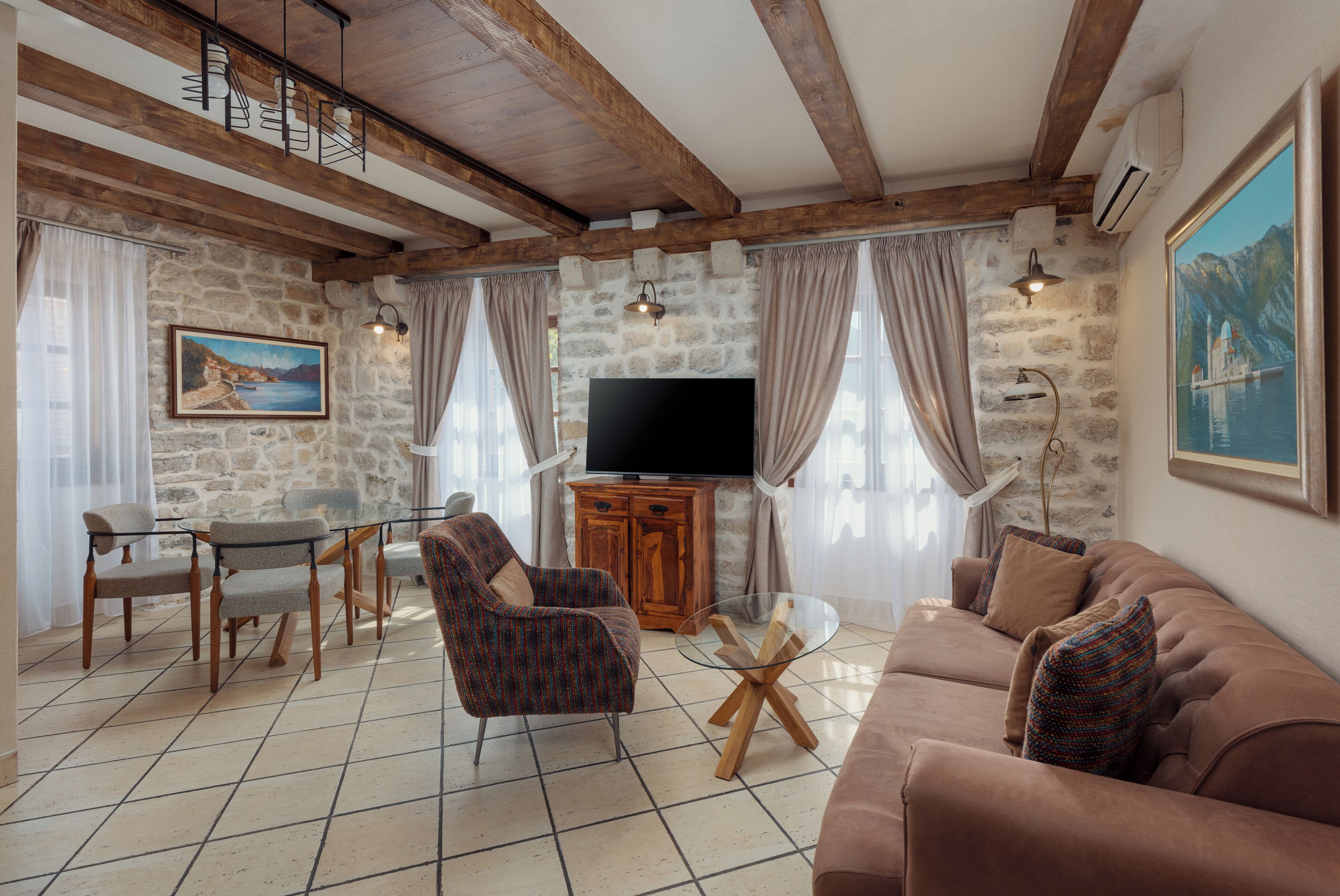 A living room with a stone wall, wooden beams, a flat-screen TV, a sofa, and a coffee table.