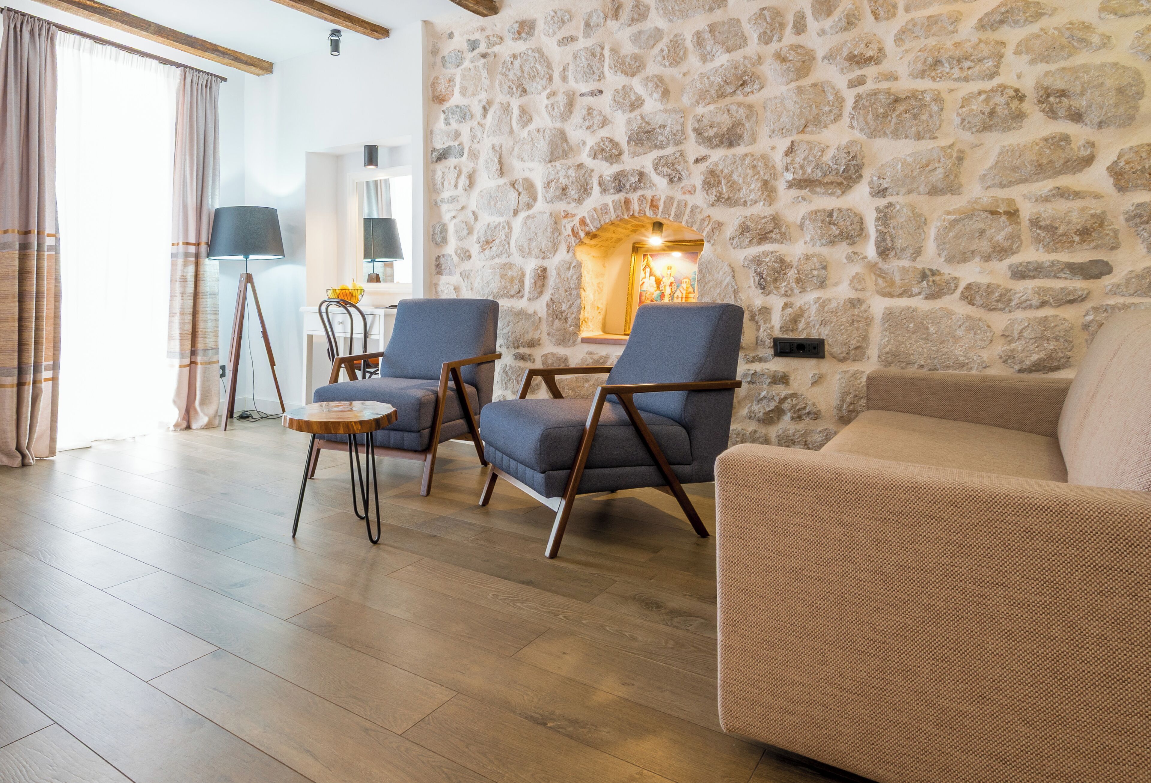 A cozy living room with a stone wall, two armchairs, a sofa, a small round table, and a lamp.