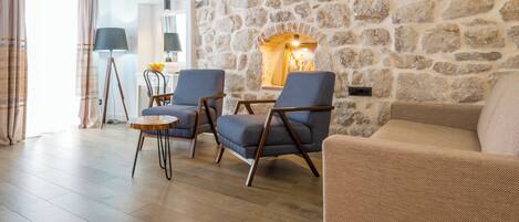 Una sala de estar acogedora con una pared de piedra, dos sillones, un sofá, una mesita redonda y una lámpara.