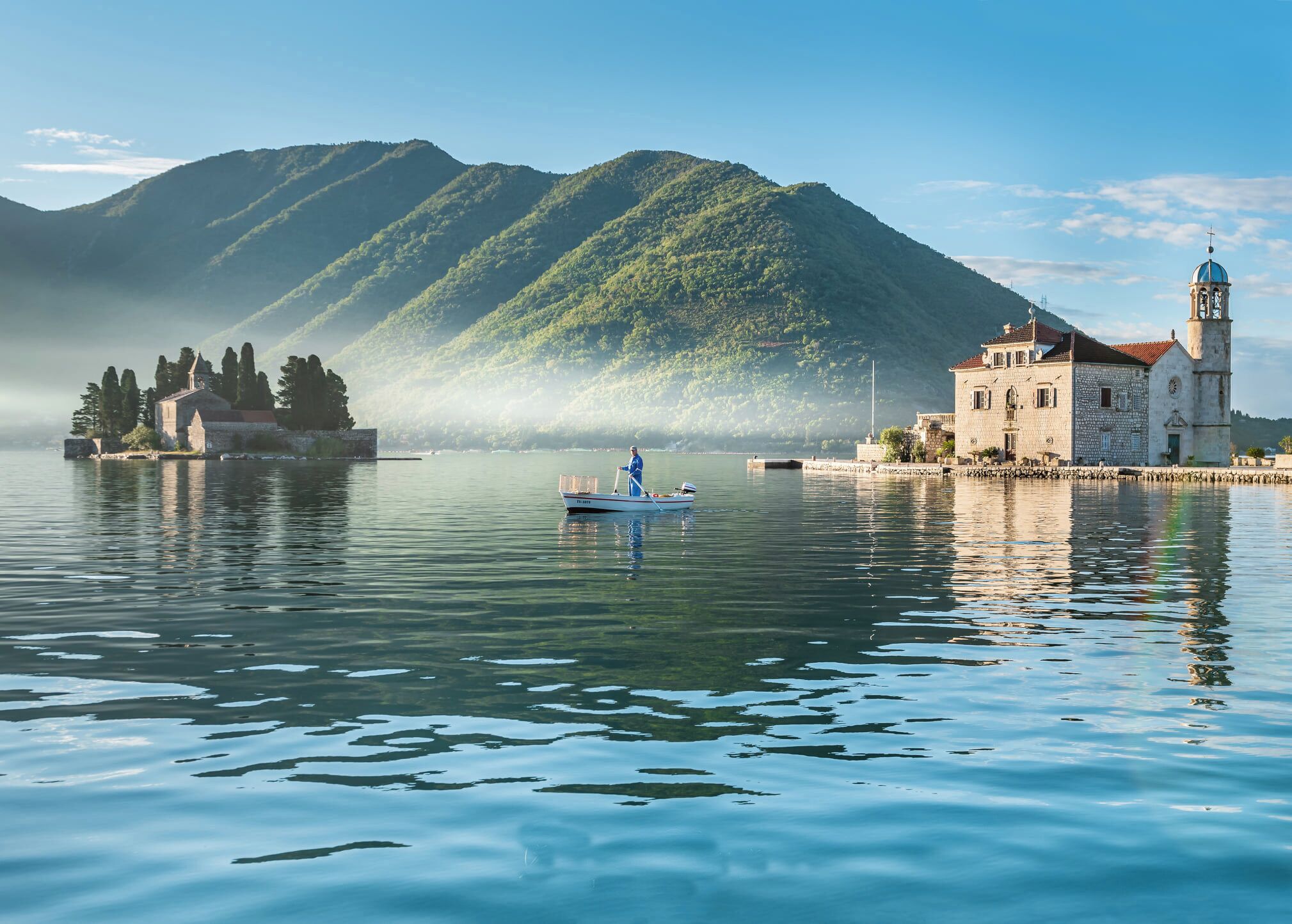 A serene lake with a boat, a historic building with a bell tower, and a mountain in the background.