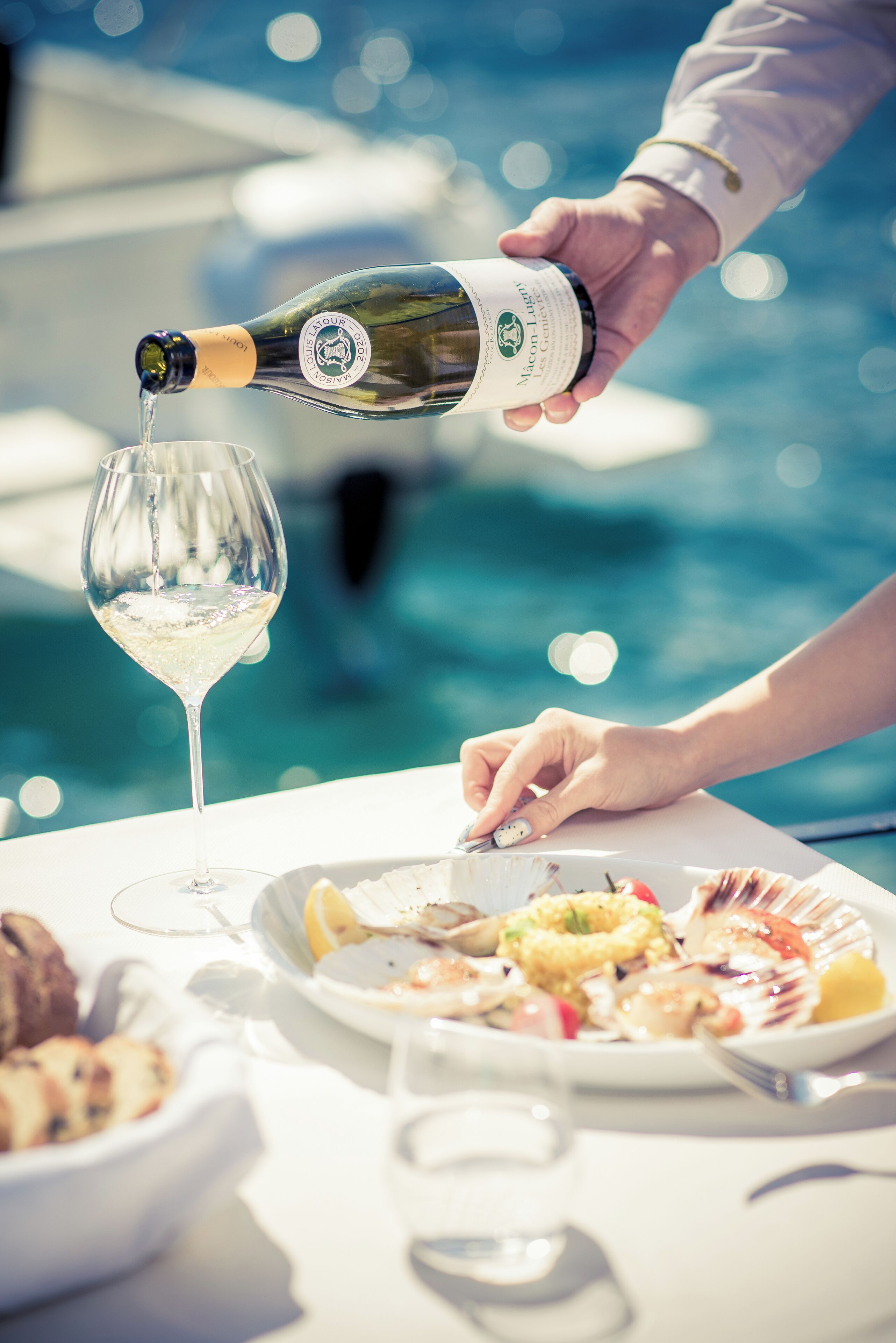 A person pouring champagne into a glass at a table by a pool.