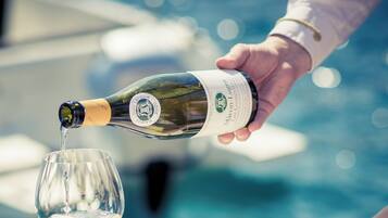 A person pouring champagne into a glass at a table by a pool.
