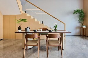 A dining area with a table set for two, wooden chairs, a staircase, and potted plants. - Jinlong Hotel (Longyan)