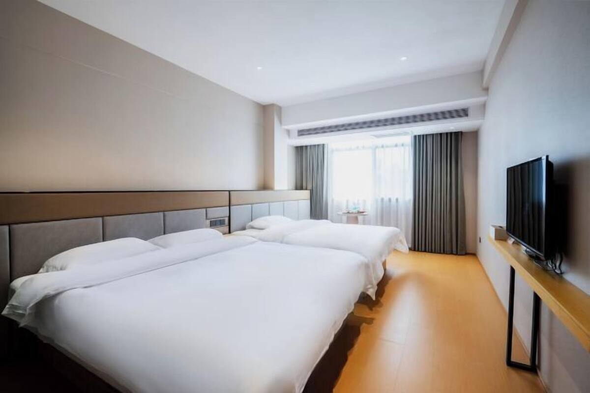 Habitación de hotel con dos camas, un televisor de pantalla plana y un ventanal con cortinas.