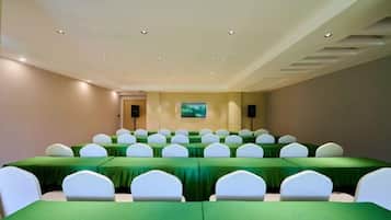 A conference room with rows of tables and chairs, a television screen, and speakers on the wall.