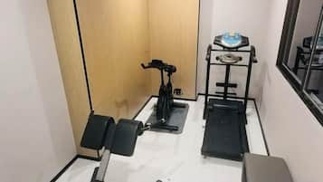 Un gimnasio pequeño con equipo de ejercicio, incluyendo una cinta de correr, bicicleta estática y banco de pesas.