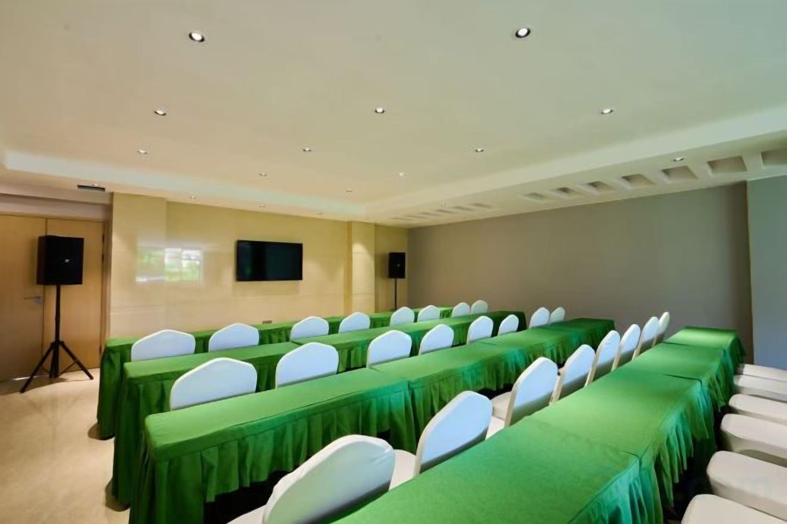 Un salón de conferencias con mesas largas, sillas blancas y una pantalla para proyector.