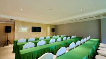 Un salón de conferencias con mesas largas, sillas blancas y una pantalla para proyector.