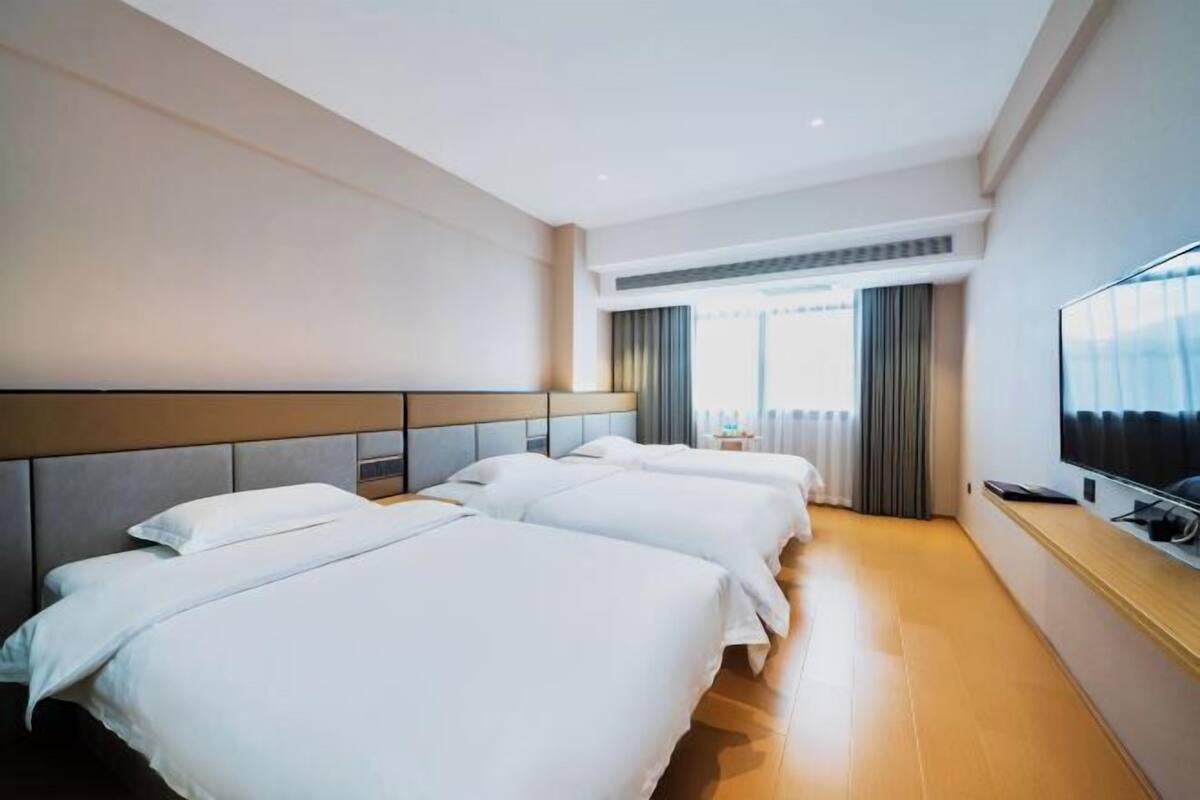 Habitación de hotel con dos camas, un televisor de pantalla plana y un ventanal grande con cortinas.