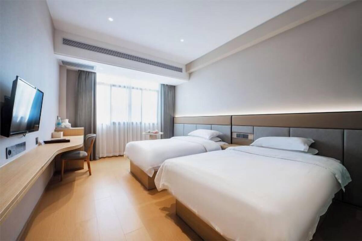 Habitación de hotel con dos camas, un escritorio, una silla, un televisor y una ventana con cortinas.