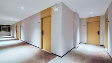 A hotel corridor with doors, carpeted floors, and a ceiling with recessed lighting.