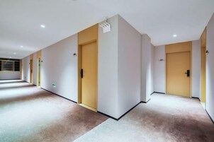 Un pasillo de hotel con puertas, pisos alfombrados e iluminación empotrada en el techo.