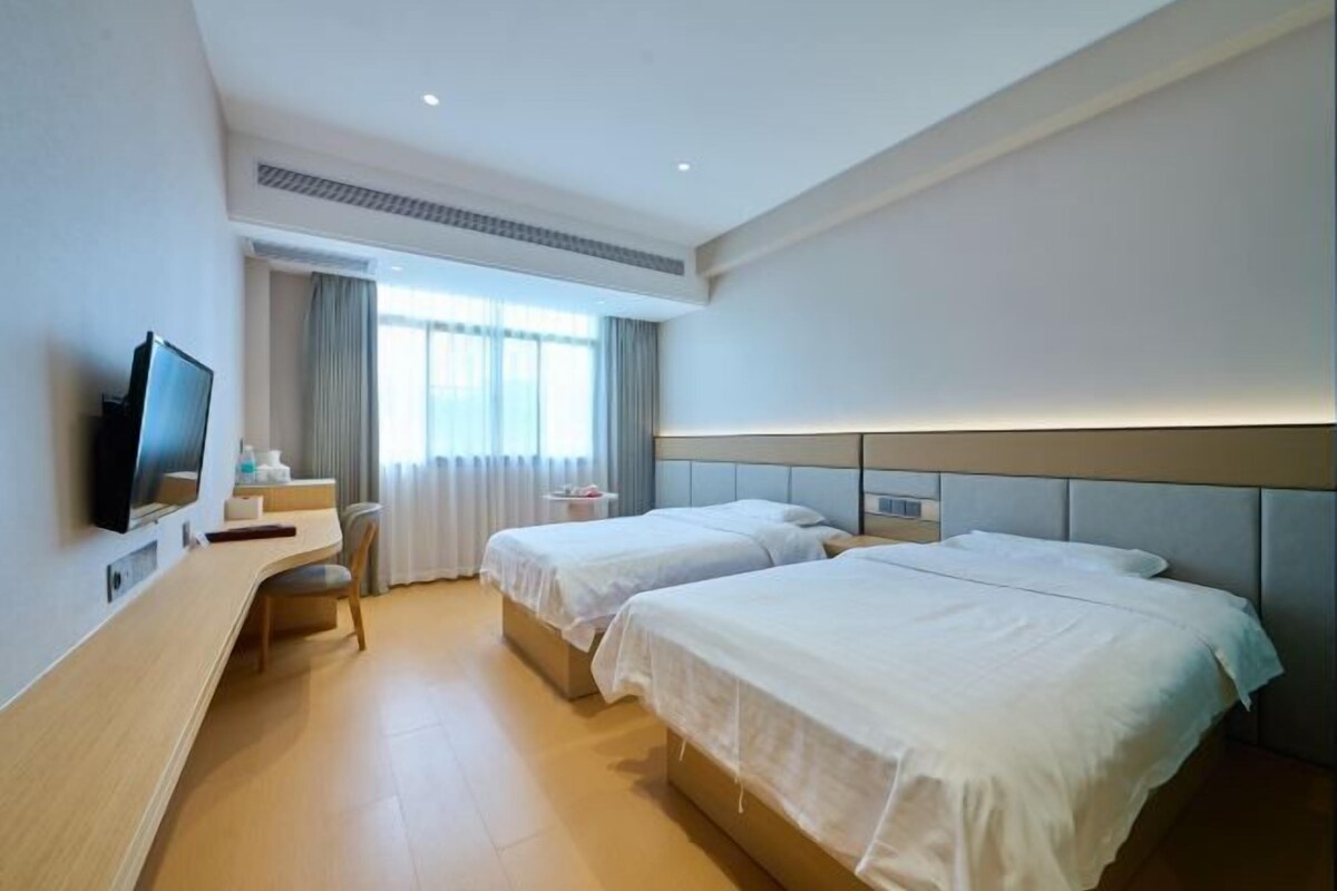A hotel room with two beds, a desk, a TV, and a window with curtains.