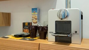 A Nespresso coffee machine on a wooden surface with a box and cups in the background. - Nice 1-bedroom apartment in Wien with WiFi (Wien)