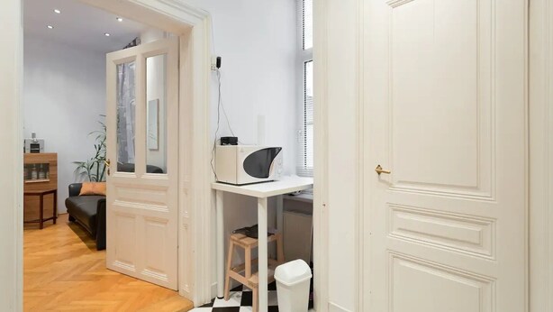 A hallway with a white door, a small table with a microwave, a trash bin, and a checkered floor. - Nice 1-bedroom apartment in Wien with WiFi (Wien)