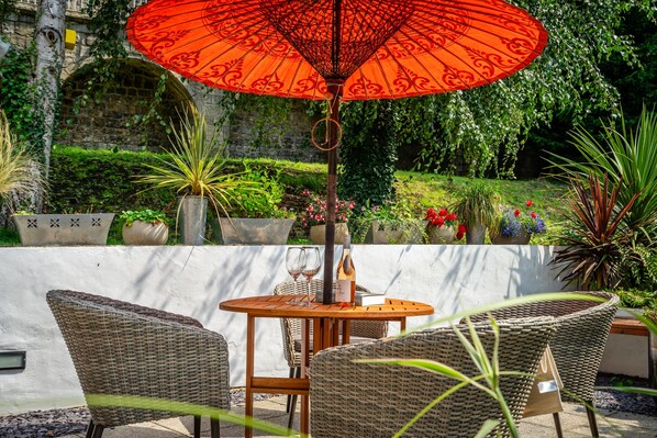An outdoor seating area with wicker chairs and a table, a red umbrella, and a wine bottle. - 16 Hunt Court - Sleeps 4 (York)