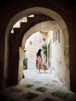 An arched corridor with a tiled floor, leading to a building with a window and a door. - Elsa D'ortigia (Syracuse)