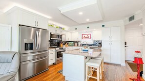 A modern kitchen with white cabinetry, stainless steel appliances, and a central island with stools.