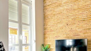 Een moderne woonkamer met een bakstenen muur, een flatscreen televisie op een witte standaard, een glazen salontafel en een bank.