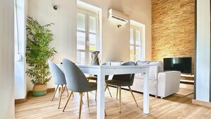 Een moderne eethoek met een witte tafel en stoelen, een plant in pot en een bakstenen muur.