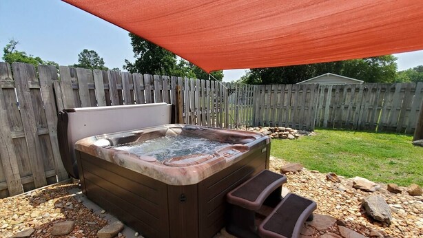 A hot tub with steps, surrounded by a wooden fence and a stone pathway.