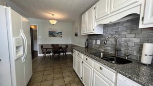 A kitchen with white cabinets, a granite countertop, a stainless steel sink, and a tiled floor.