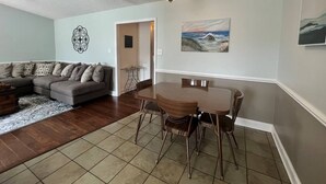 A living room with a gray sofa, a wooden dining table with chairs, a patterned rug, and a ceiling light.