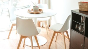 Een lichte eetruimte met een ronde tafel, witte stoelen en een plafondventilator.