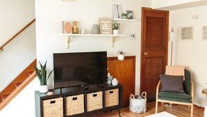 Een woonkamer met een televisie, houten kasten, rieten manden, een groene fauteuil en een houten deur.