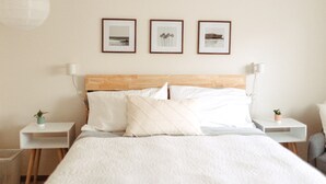 Een keurig opgemaakt slaapkamer met een houten hoofdbord, een bed met witte lakens, en drie ingelijste foto’s aan de muur.