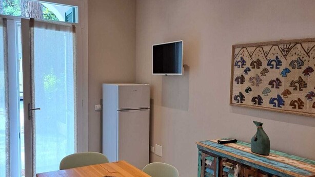 Ein Essbereich mit Holztisch, Stühlen, einem Kühlschrank, einem an der Wand befestigten Fernseher und einem farbenfrohen Schrank.