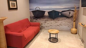 A room with a red sofa, a small round table, a large beach-themed mural, and a vase with dried plants. - Marina Romea 2 Splitted Executive Flats (Ravenna)