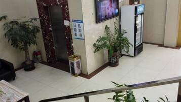 A reception area with a marble reception desk, a television mounted on the wall, a refrigerator, and potted plants.