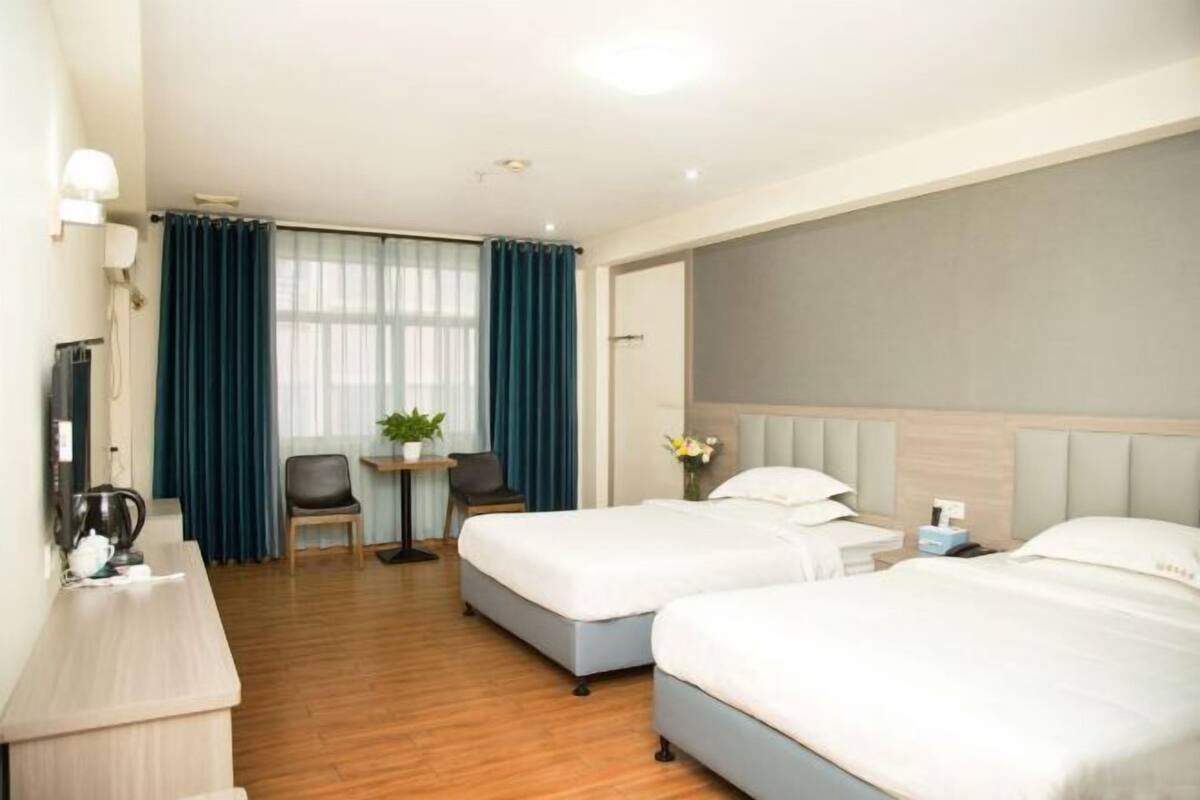 A hotel room with two beds, a desk, a chair, and a small table with a plant.