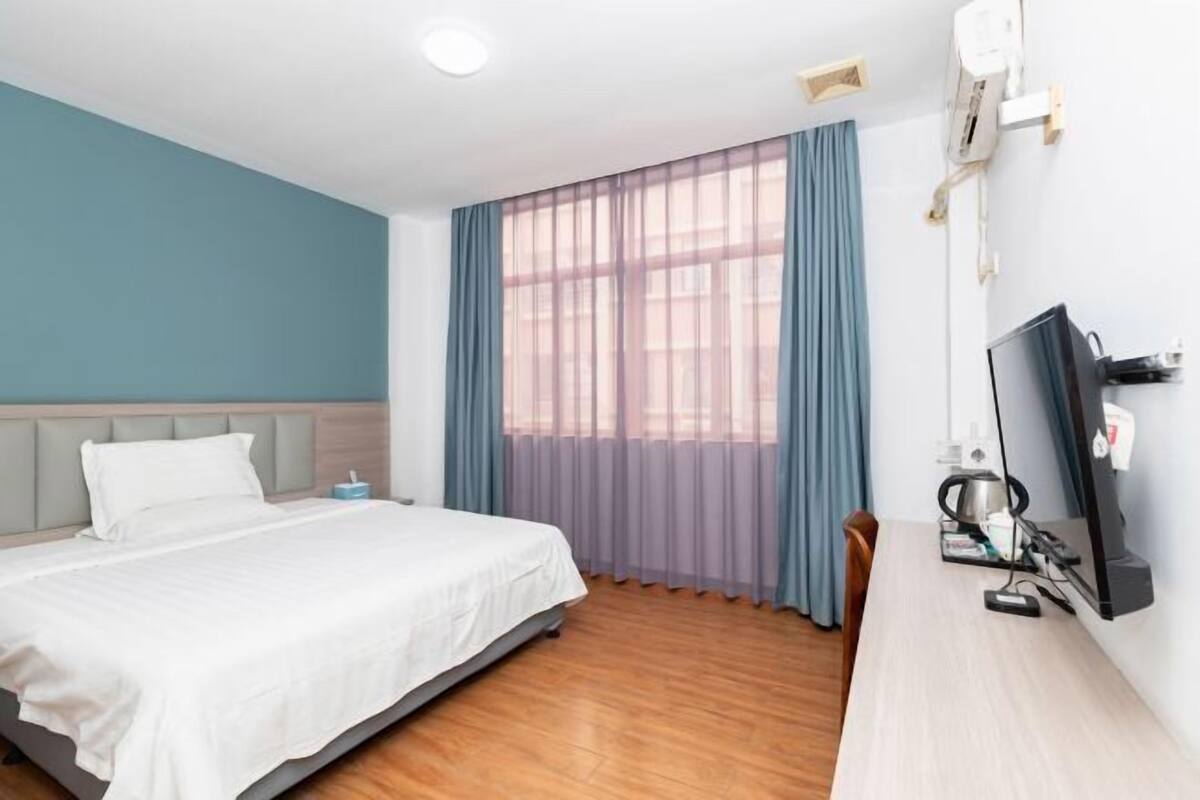 A hotel room with a bed, a desk with a computer, and a window with curtains.