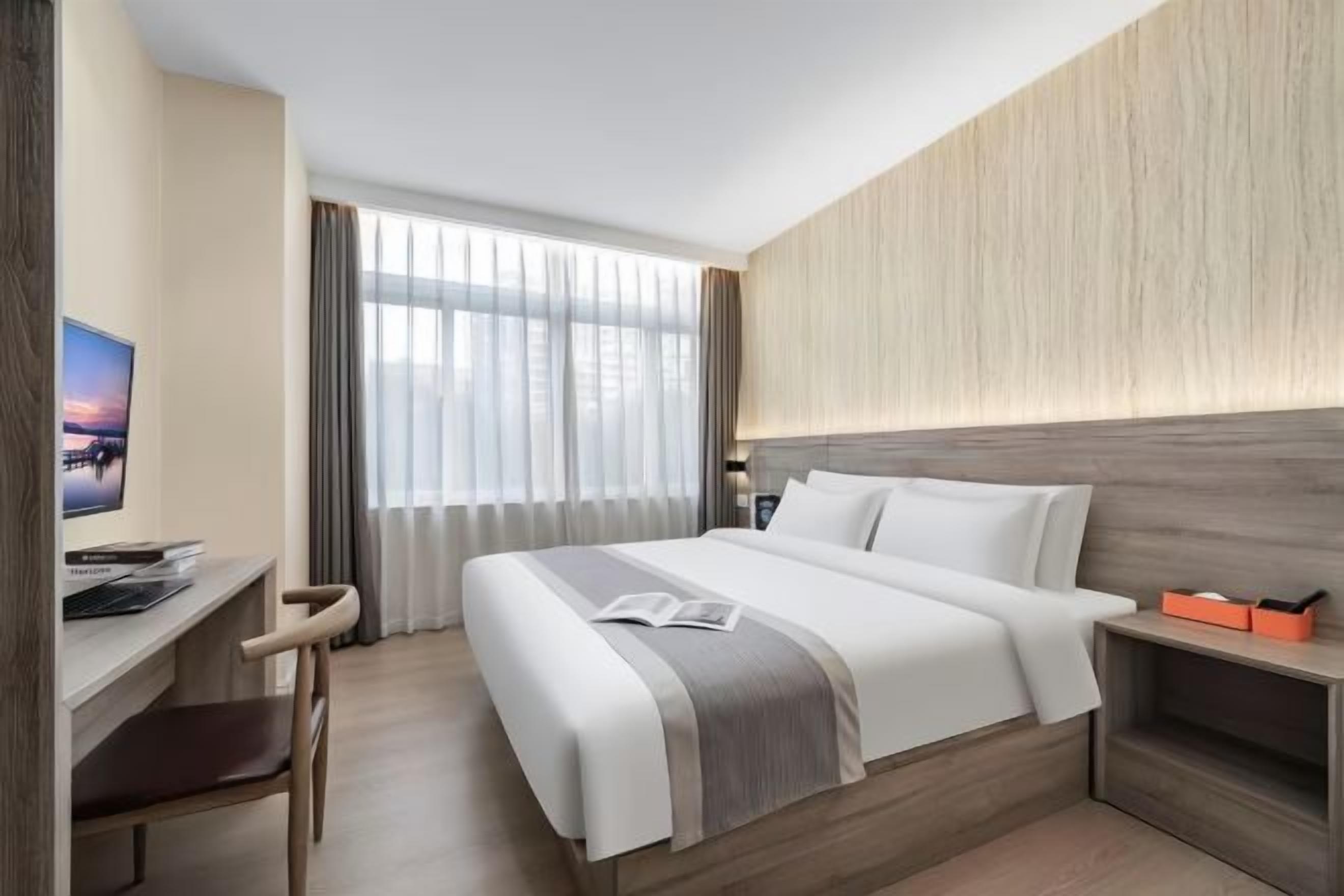 Quarto de hotel com cama, escrivaninha, cadeira e televisão.