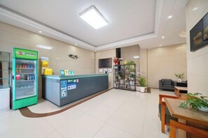 A hotel reception area with a reception desk, a green vending machine, and a seating area with a table and chairs. - Shenzhen Liuliu Hotel (Shiyan Bus Station) (Shenzhen)