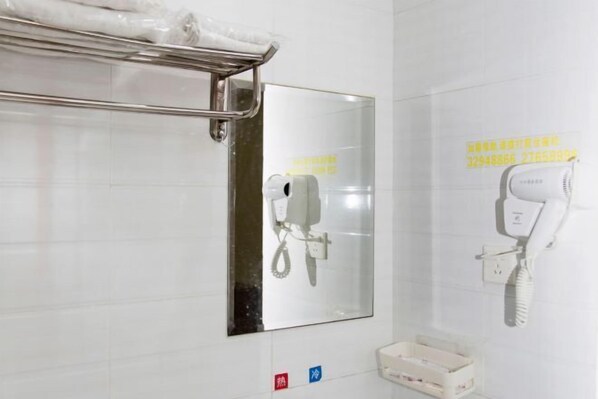 Casa de banho com secador de mãos, espelho e um pequeno contentor de lixo.