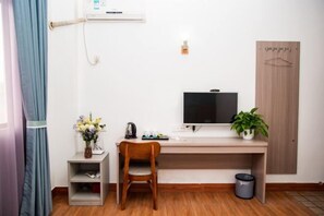 A small, compact room with a wooden desk, a chair, a television, a small shelf with a vase, and a potted plant. - Shenzhen Liuliu Hotel (Shiyan Bus Station) (Shenzhen)