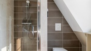 Een moderne badkamer met een douche met glazen wand, een toilet en een klein opbergruimte.